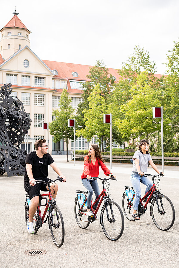 Drei junge Menschen fahren auf Fahrrädern durch die Stadt.