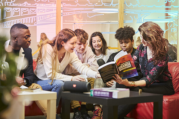 Junge Menschen sitzen um einen kleinen Tisch und schauen gemeinsam in ein Buch
